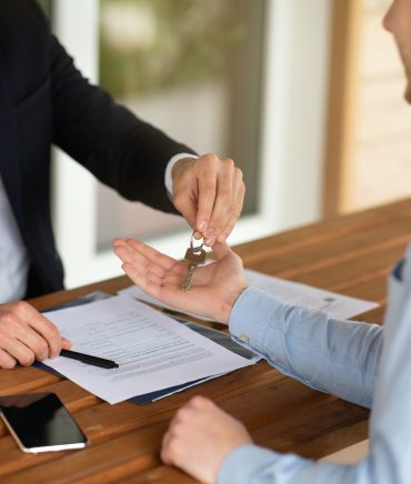 Closeup view of real estate agent giving house keys to male client at table