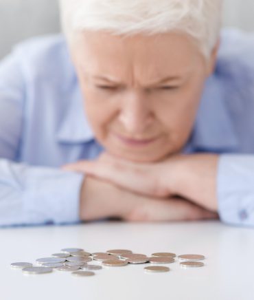 Elderly Poverty. Depressed senior woman looking at last coins lying at table